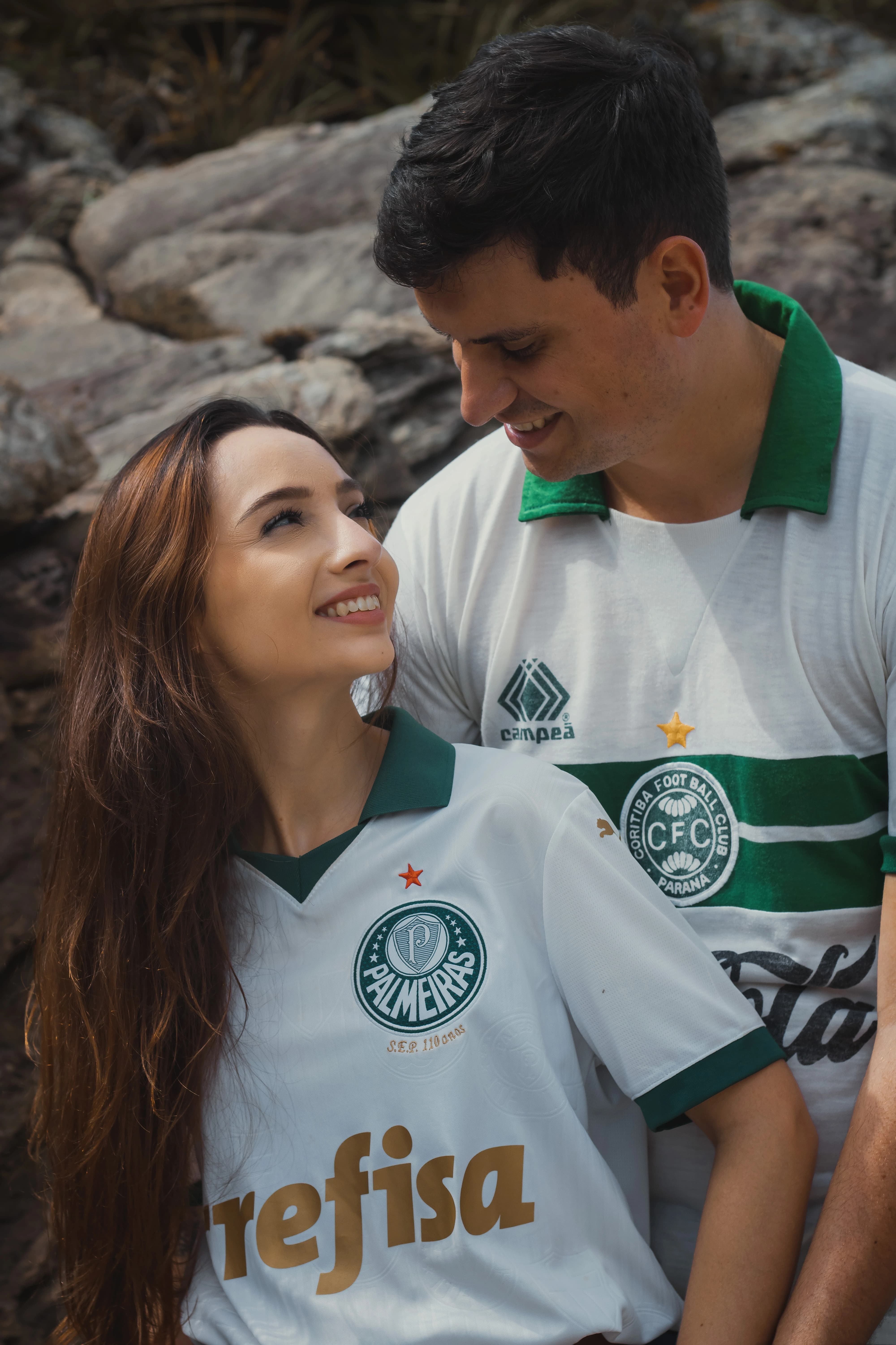 Os noivos se encaram sorrindo, com os rostos próximos. A noiva veste a camiseta mais recente do Palmeiras, enquanto o noivo usa uma camiseta retrô do Coritiba.