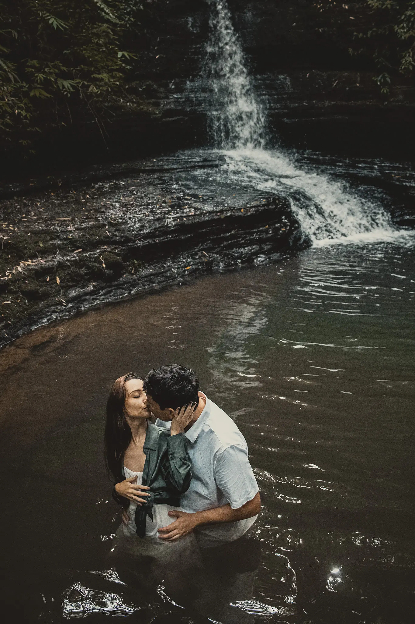 Noivos se beijando dentro de cachoeira com cascata ao fundo