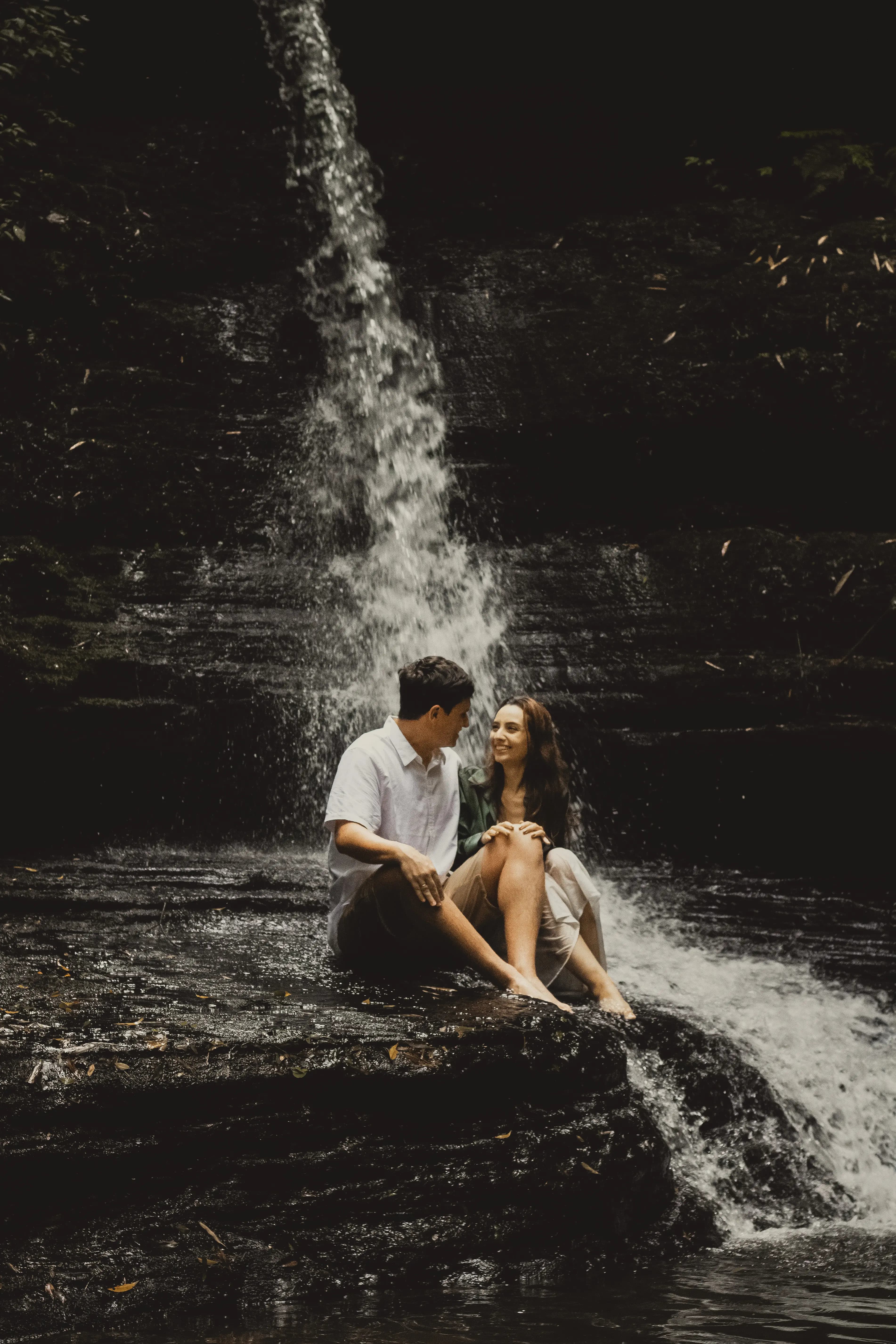 Noivos sentados em pedra de cachoeira com cascata ao fundo