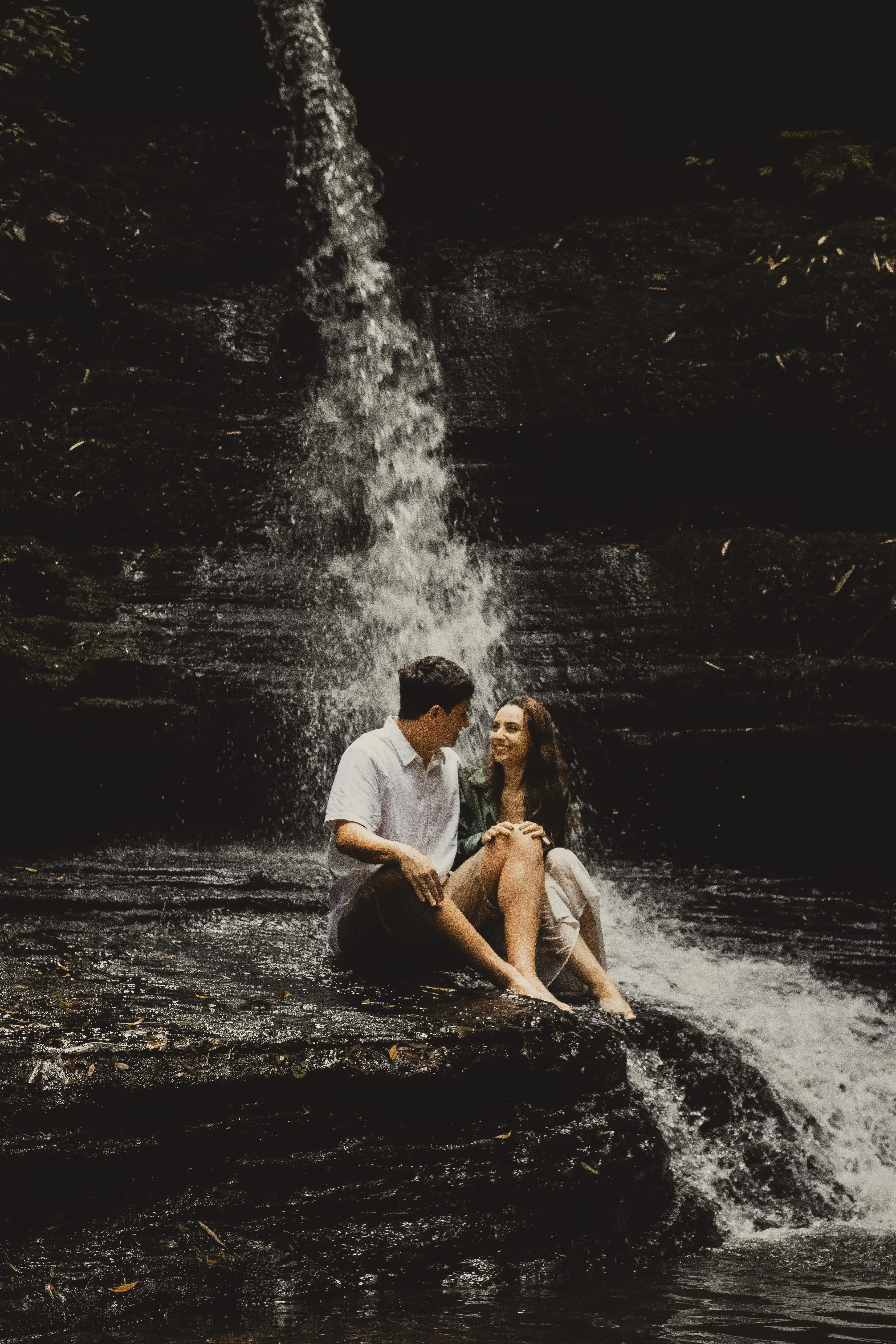 Noivos sentados em pedra de cachoeira com cascata ao fundo